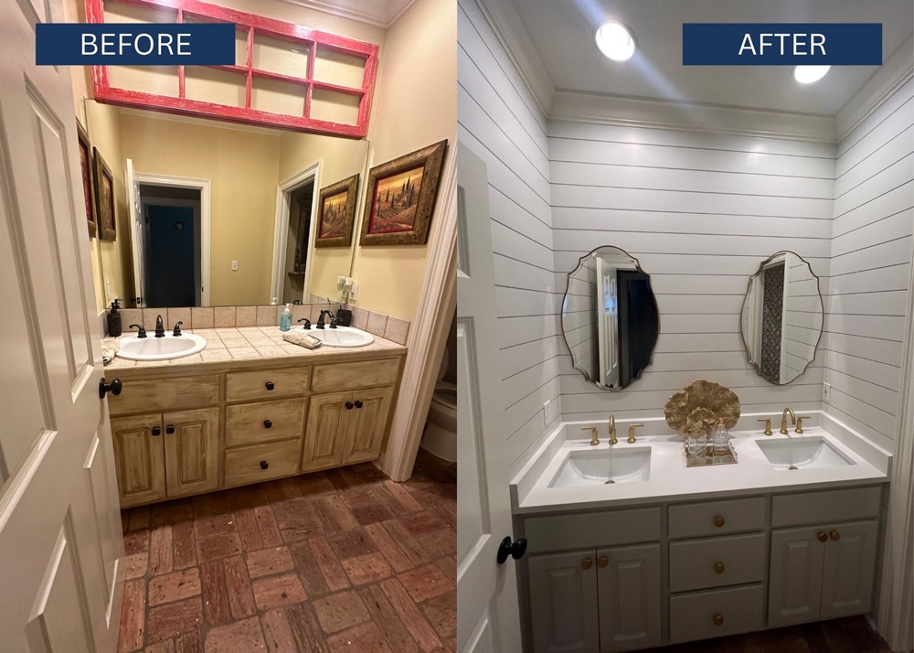 Before: beige walls, wood double-sink vanity with tiled countertop, red-framed open mirror above, and wall art on the right-side wall in a doorway-framed bathroom.